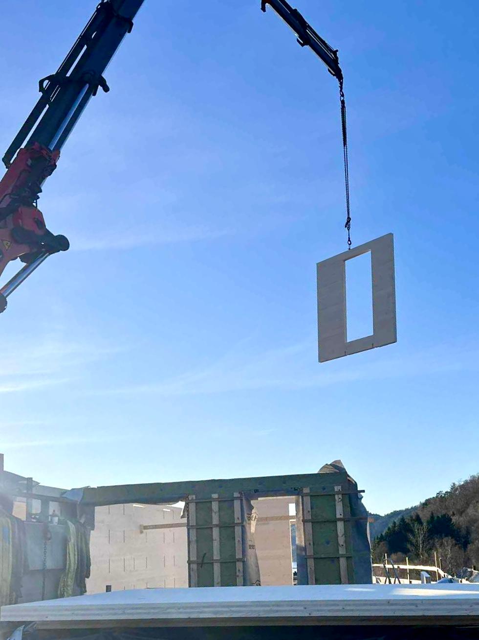 Veggelement i massivtre med vindusåpning heises på plass med kran