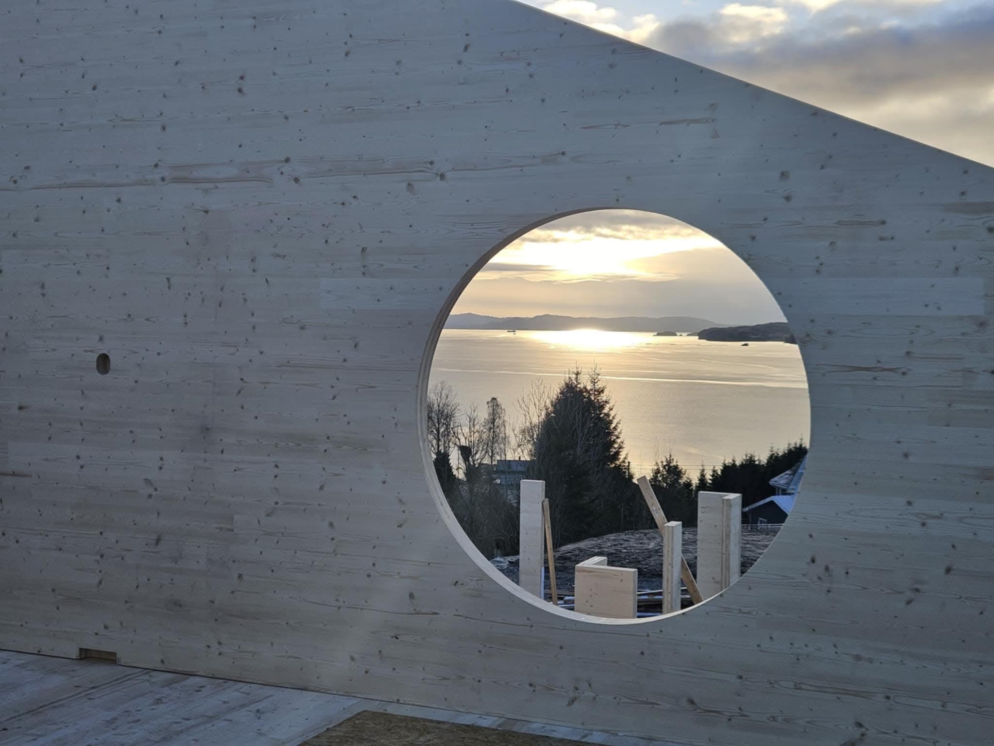 Rundt vindu i en ny vegg, med utsikt over fjorden i solnedgang